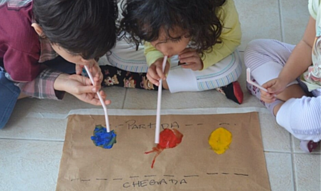 Crianças pintam com recurso a uma palhinha que seguram com a boca
